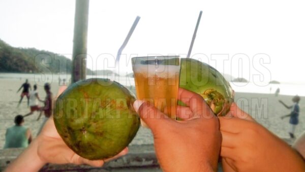 Three hand holding coconuts and glass of beer on the beach