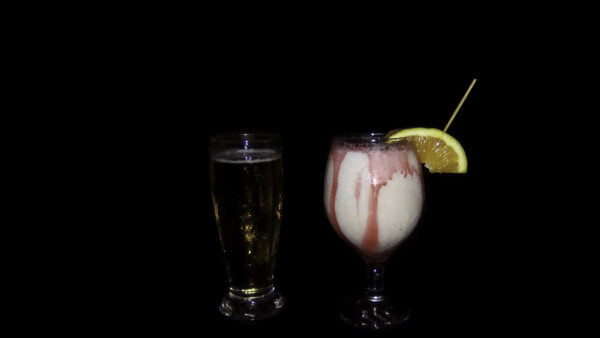 Beer and strawberry drink with orange on black background