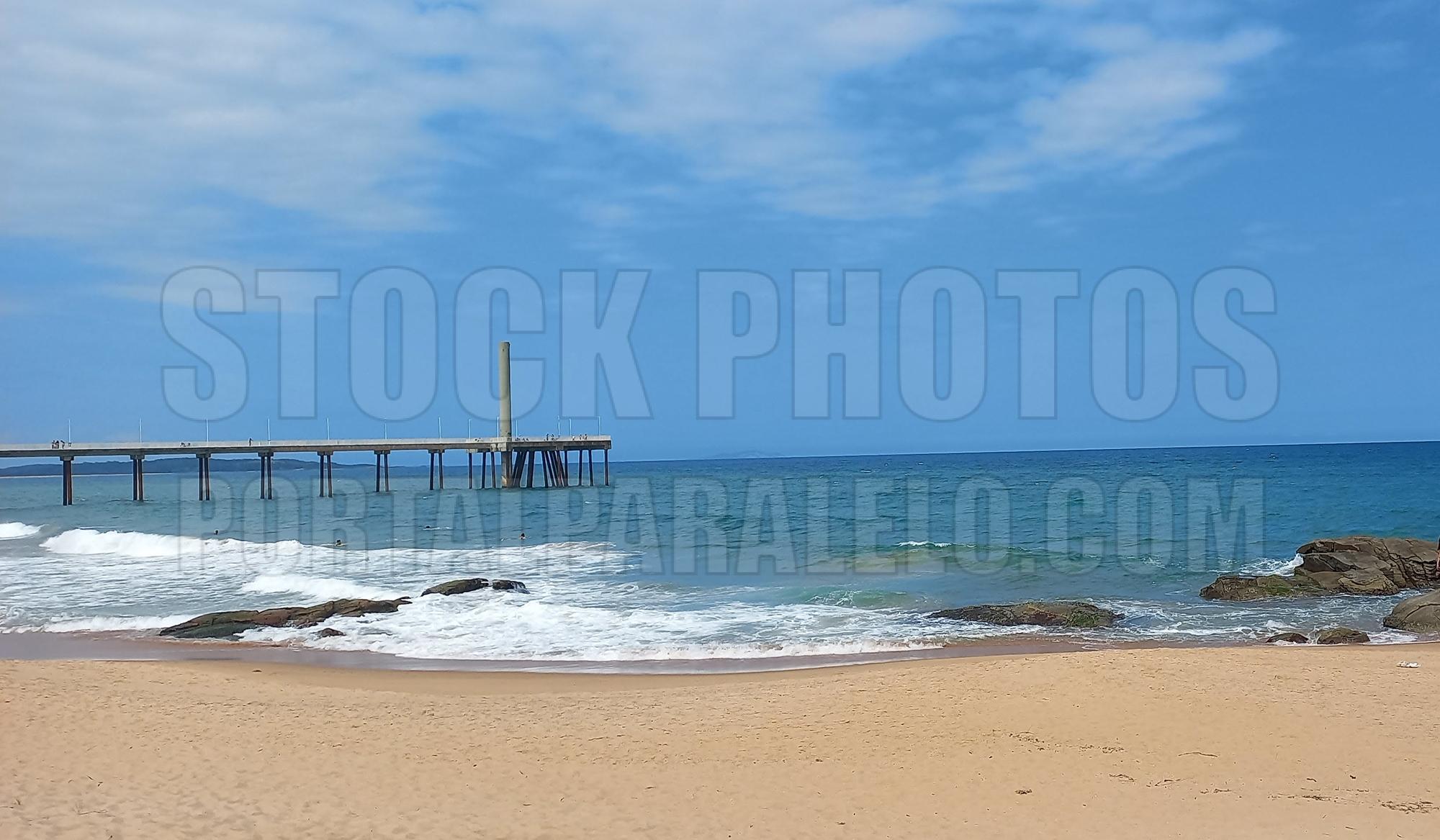 Beach with golden sand, blue sky and an underwater outfall in the background.